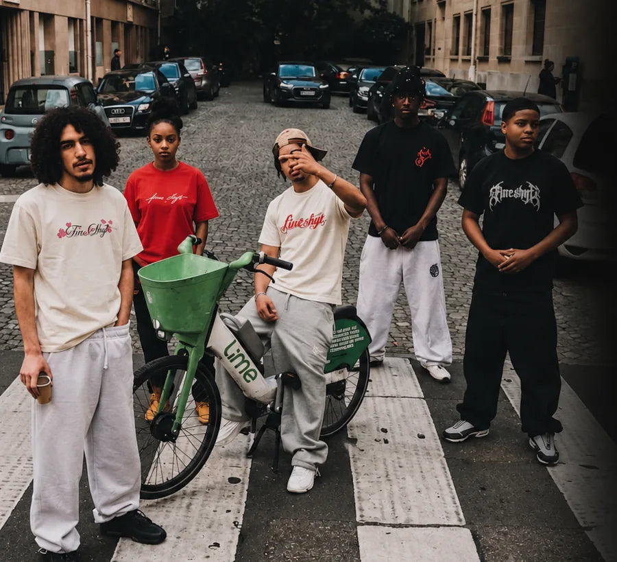 Six people in Fine Shyt tees standing at a cobbled street crossing